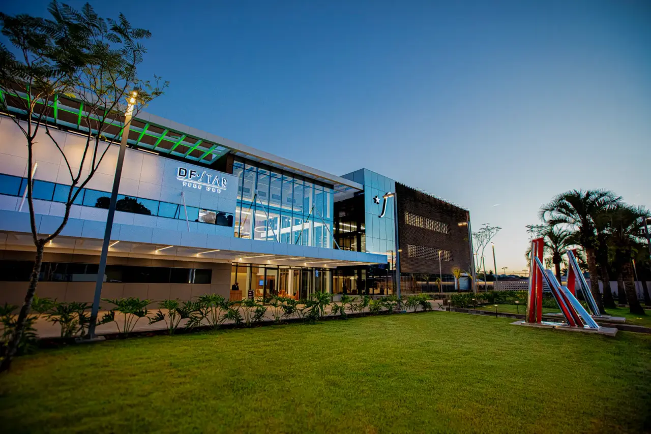 Fachada de vidro do DF Star ao entardecer, com jardim na frente